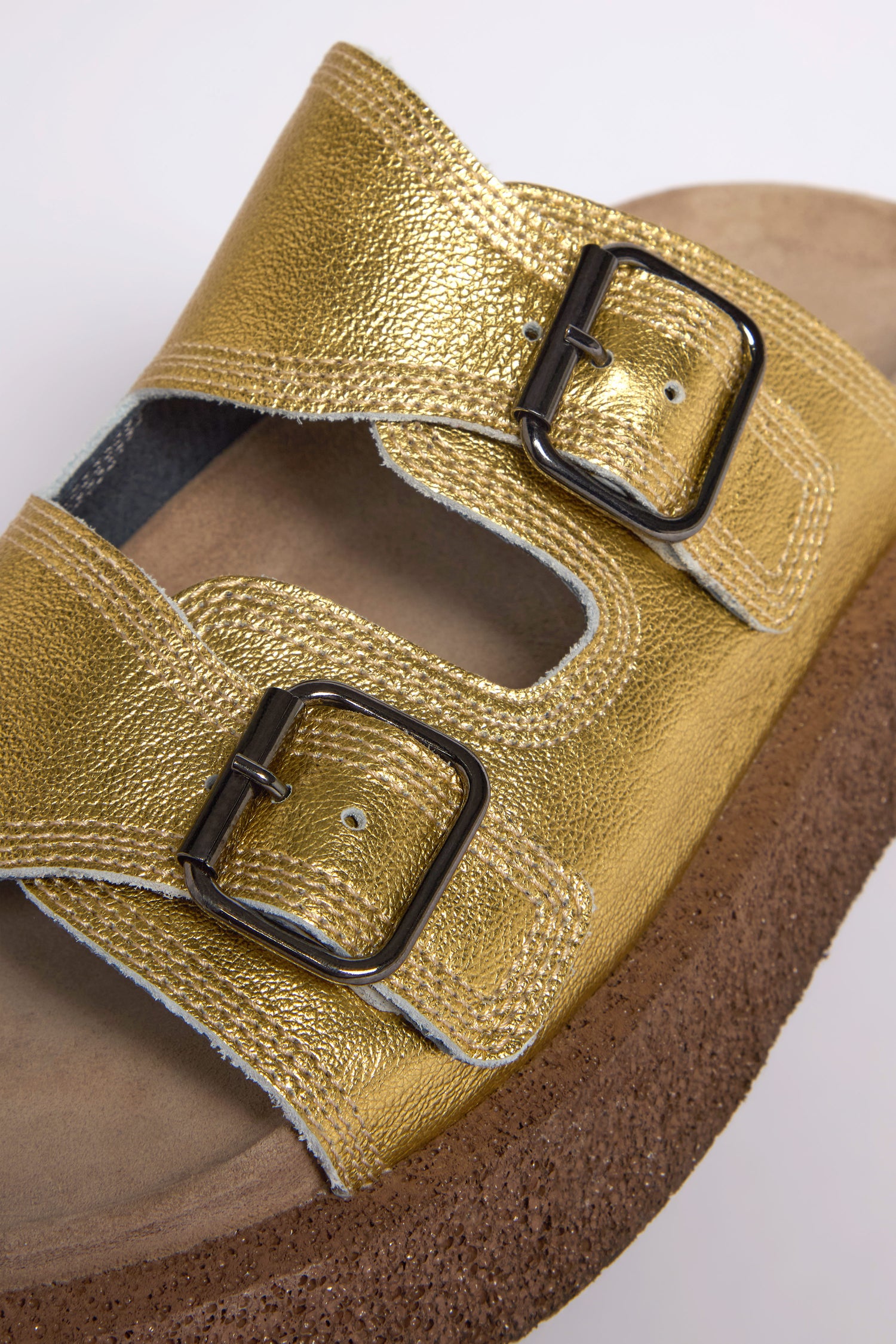 A close-up of the Metallic Gold Double Buckle Leather Sliders, showcasing two buckled straps and a cork sole, expertly handcrafted in Italy.