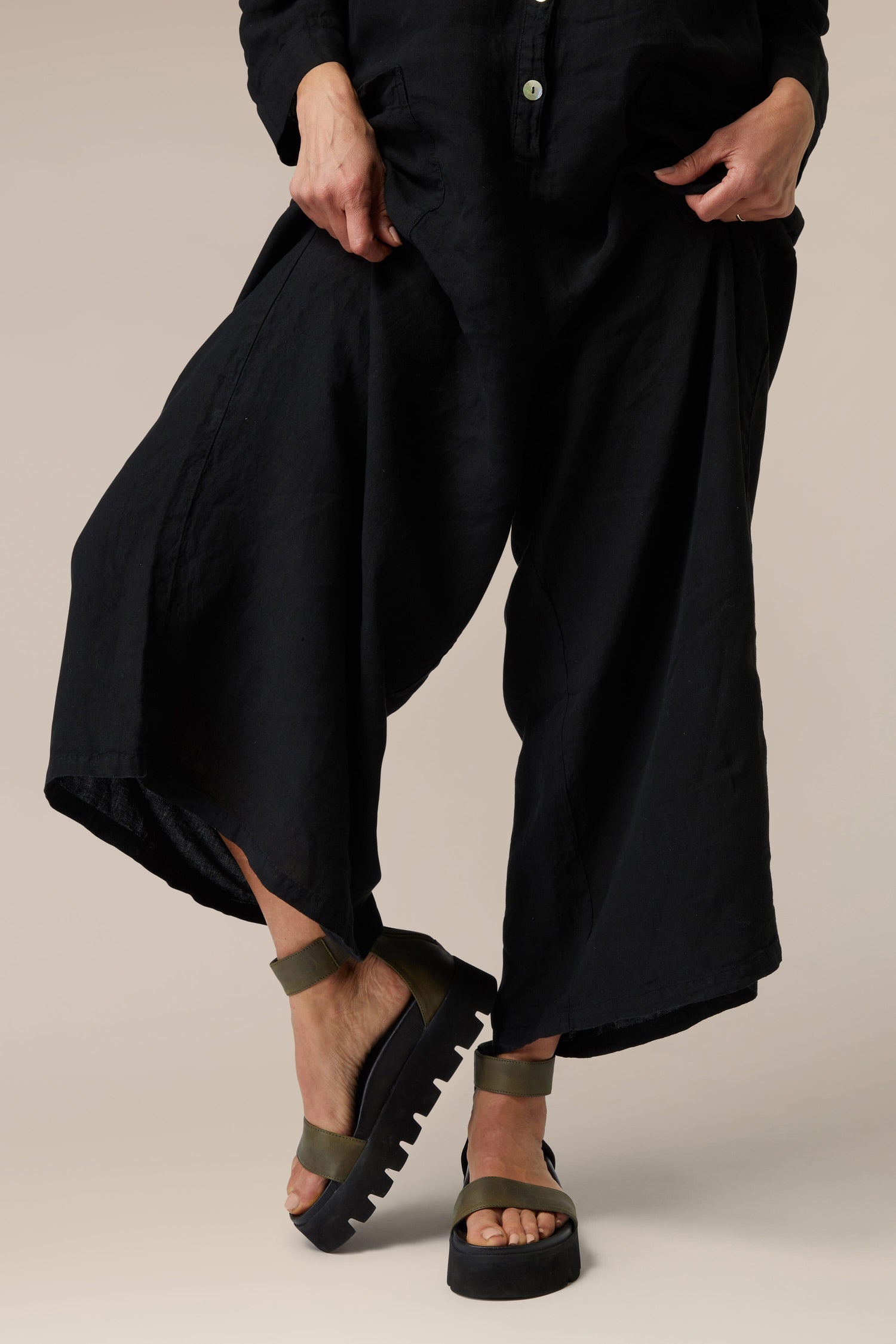 Person standing in black wide-leg pants and olive green Leather Platform Zip Sandals.