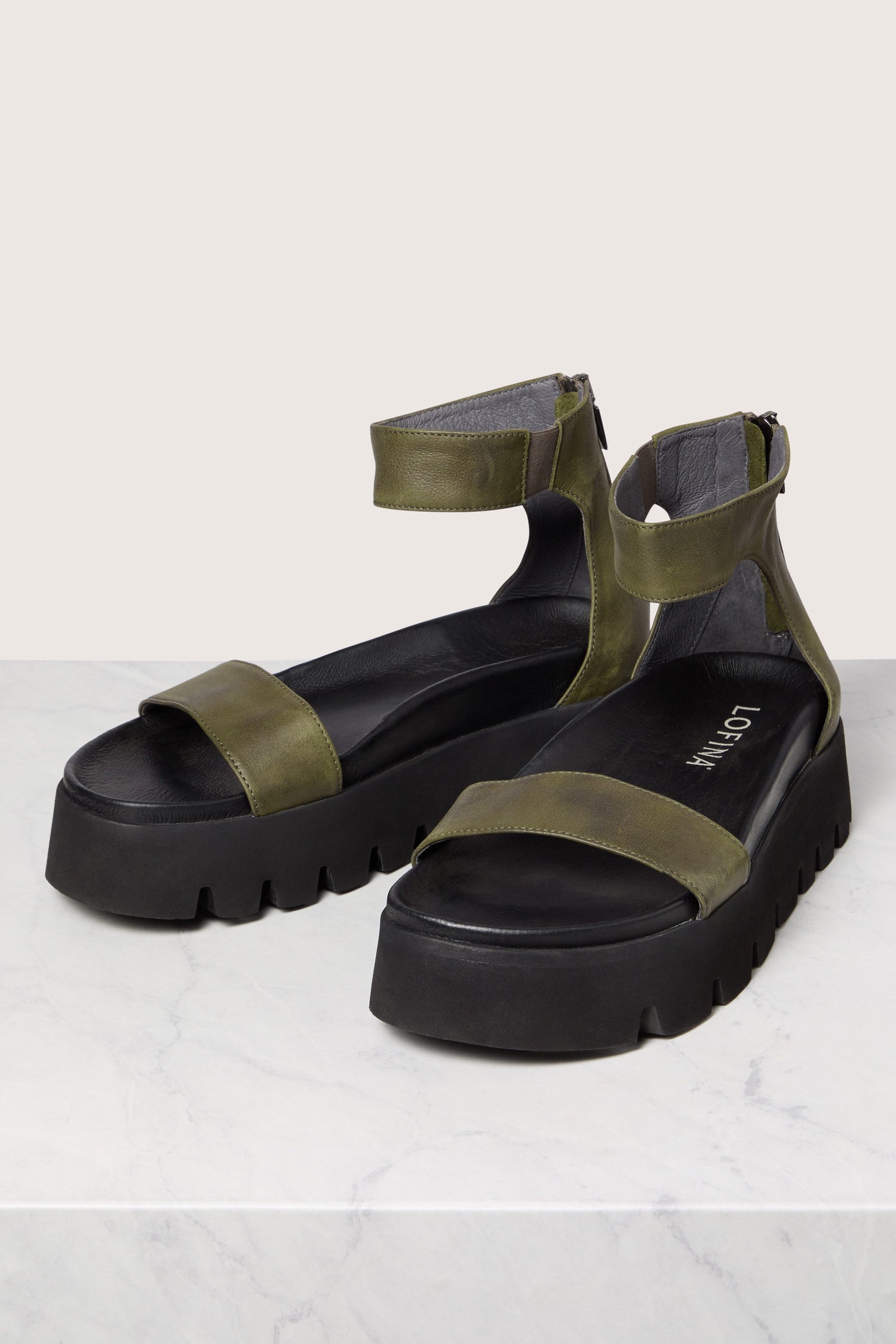 A pair of Leather Platform Zip Sandals in olive green, featuring handmade Italian construction, displayed on a marble surface.