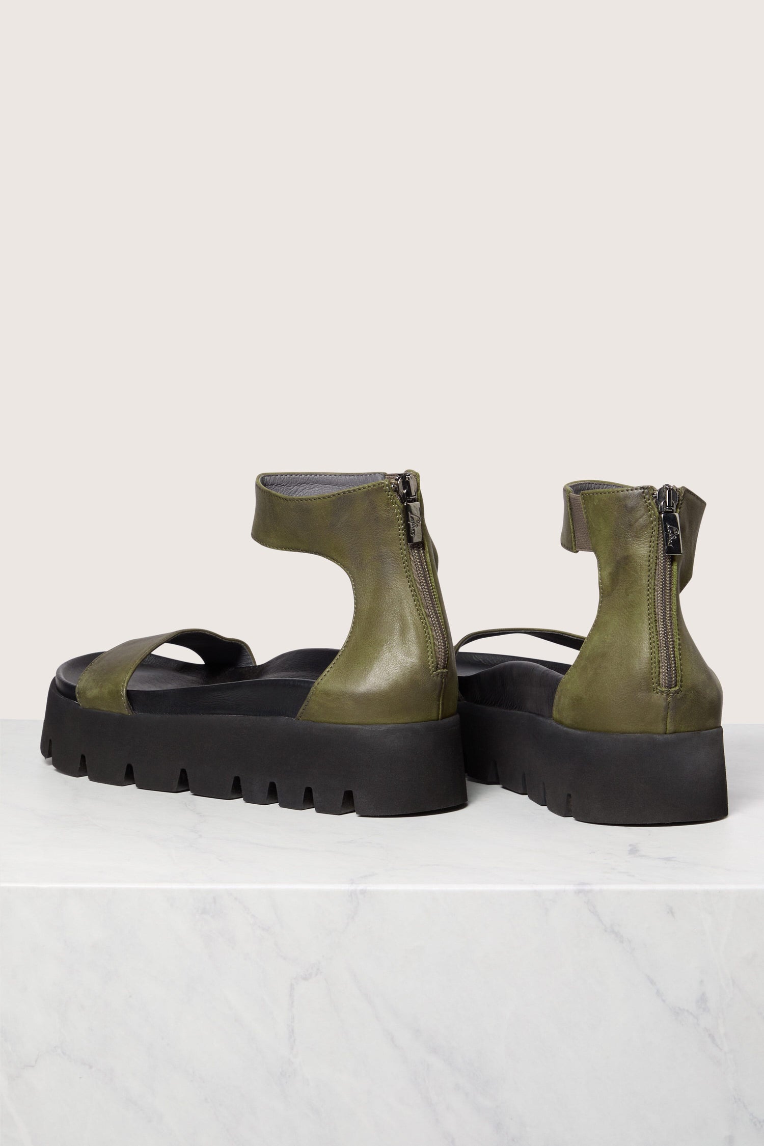 A pair of Olive Green Leather Platform Zip Sandals with zippers on a marble surface, featuring handmade Italian construction.