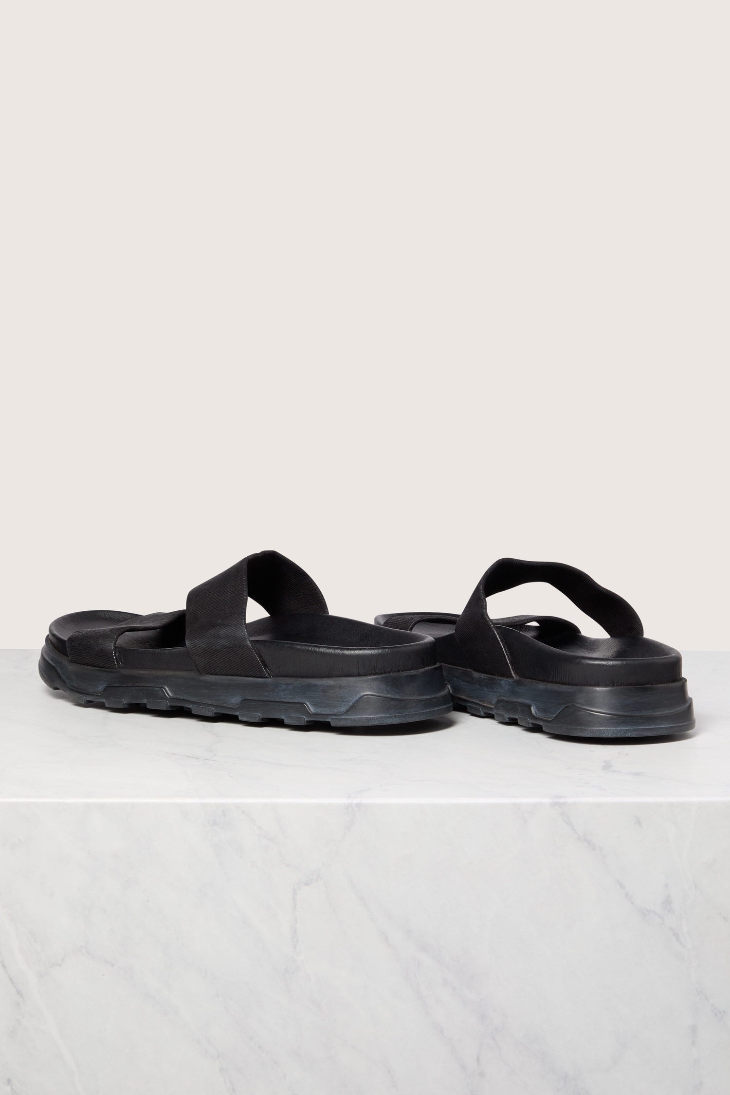 Black Stretch Leather Slider sandals on a white marble surface.
