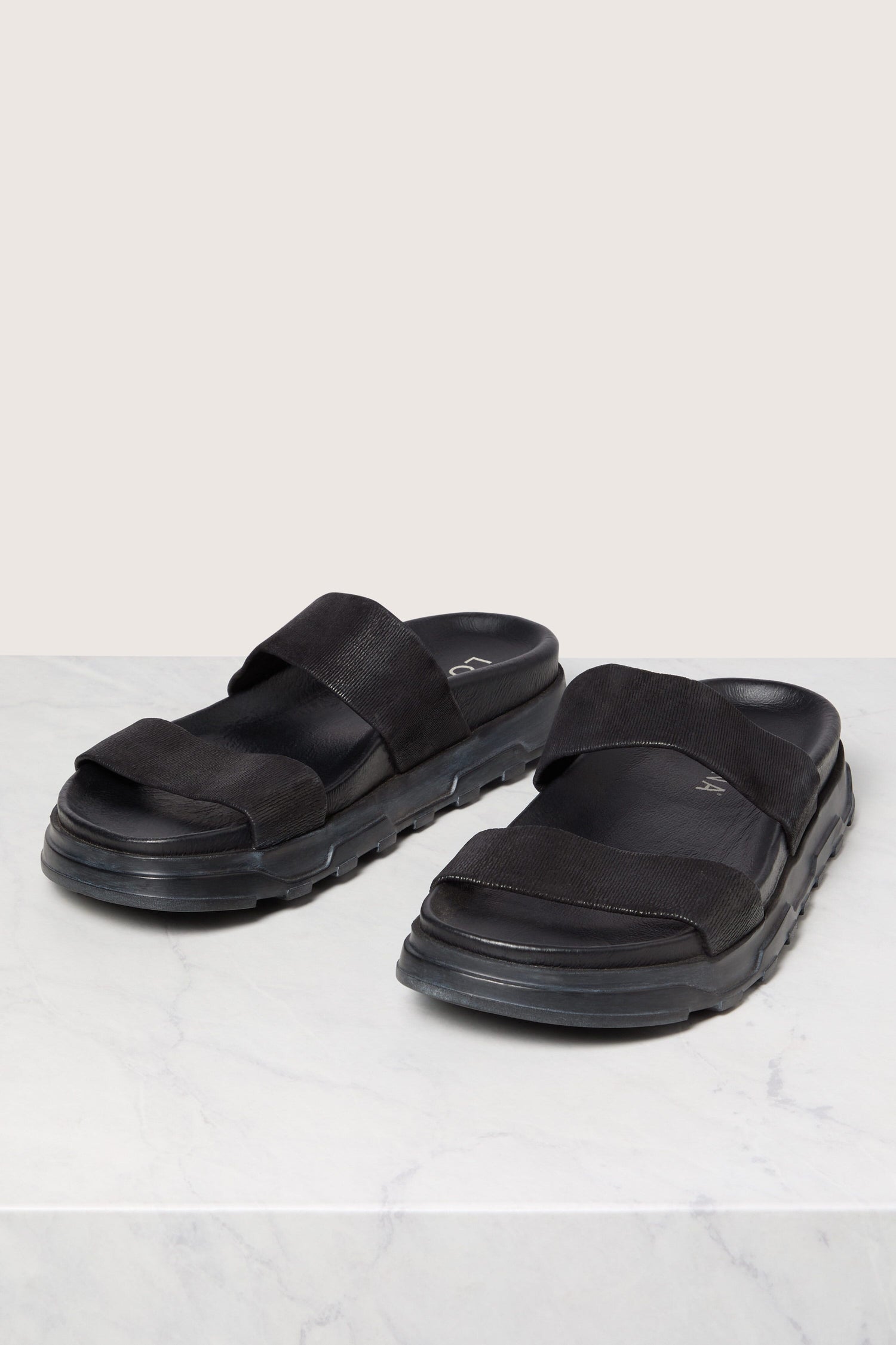 A pair of Italian construction black Stretch Leather Sliders on a white surface.