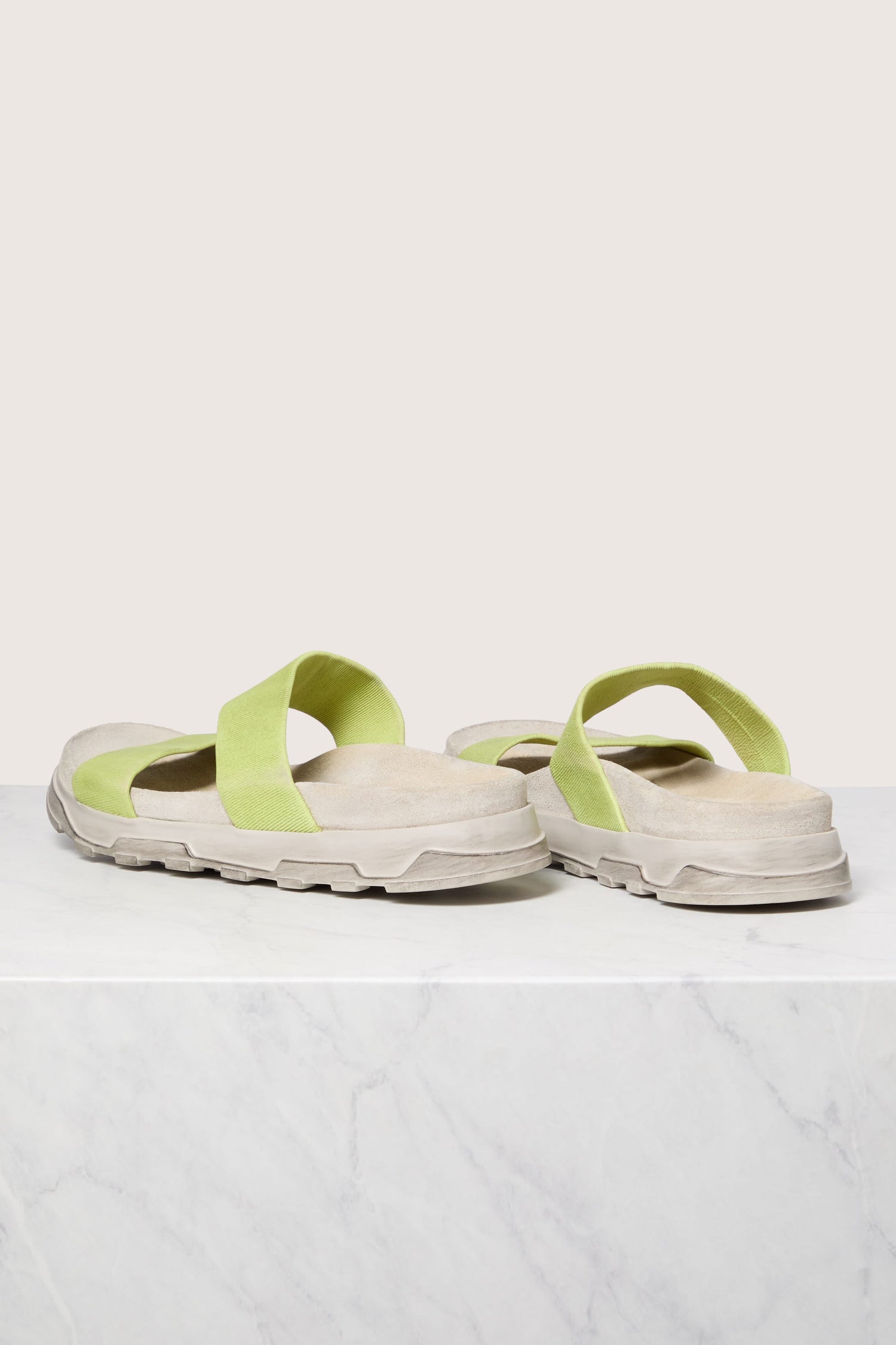 Sentence with product name: A pair of light green Stretch Leather Slider sandals on a white marble surface, featuring Italian construction.