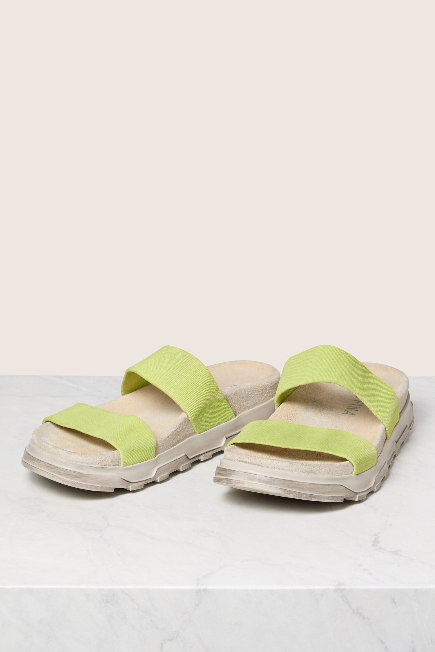 Sentence with Product Name: A pair of lime green Hawai Leather Slider sandals on a white surface with a Scandinavian design-inspired neutral background.