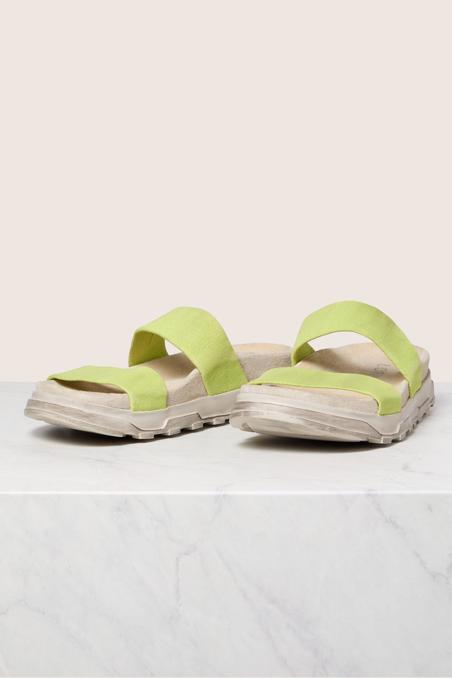 A pair of green Hermès Oran sandals on a white surface against a neutral background.