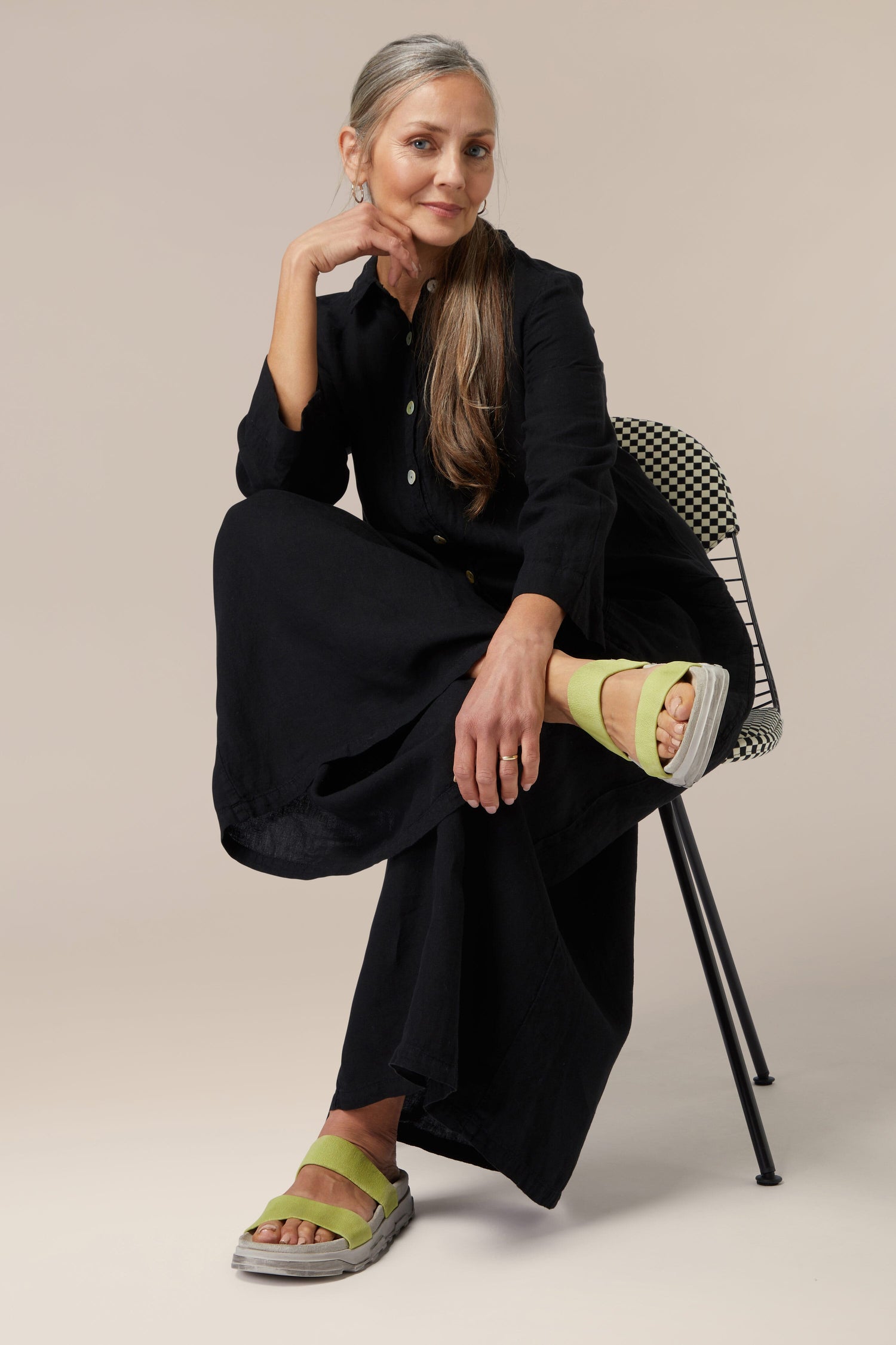 A woman in a Stretch Leather Slider outfit sitting on a Scandinavian design chair against a neutral background.