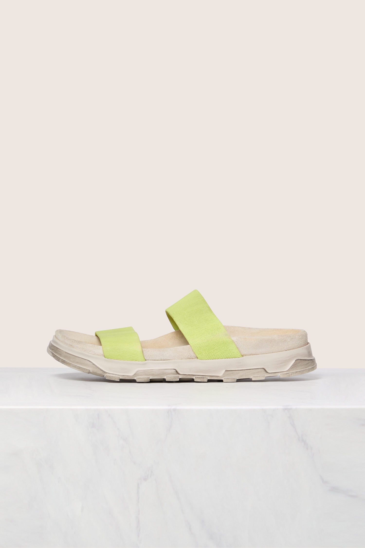 A pair of lime green Stretch Leather Slider sandals on a white surface with a marble pattern, showcasing Scandinavian design.