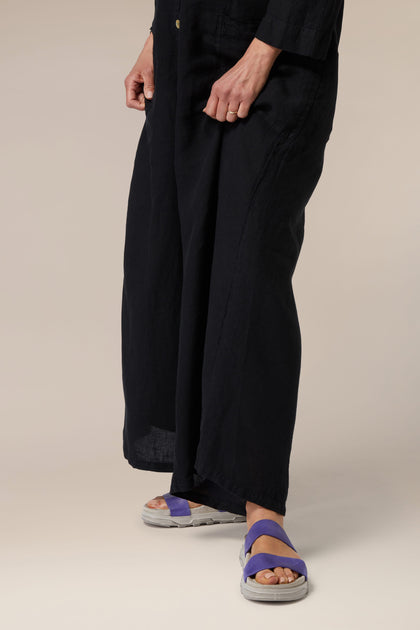 A person standing in a pair of navy blue wide-leg pants and Stretch Leather Sliders, featuring Italian construction, against a beige background.