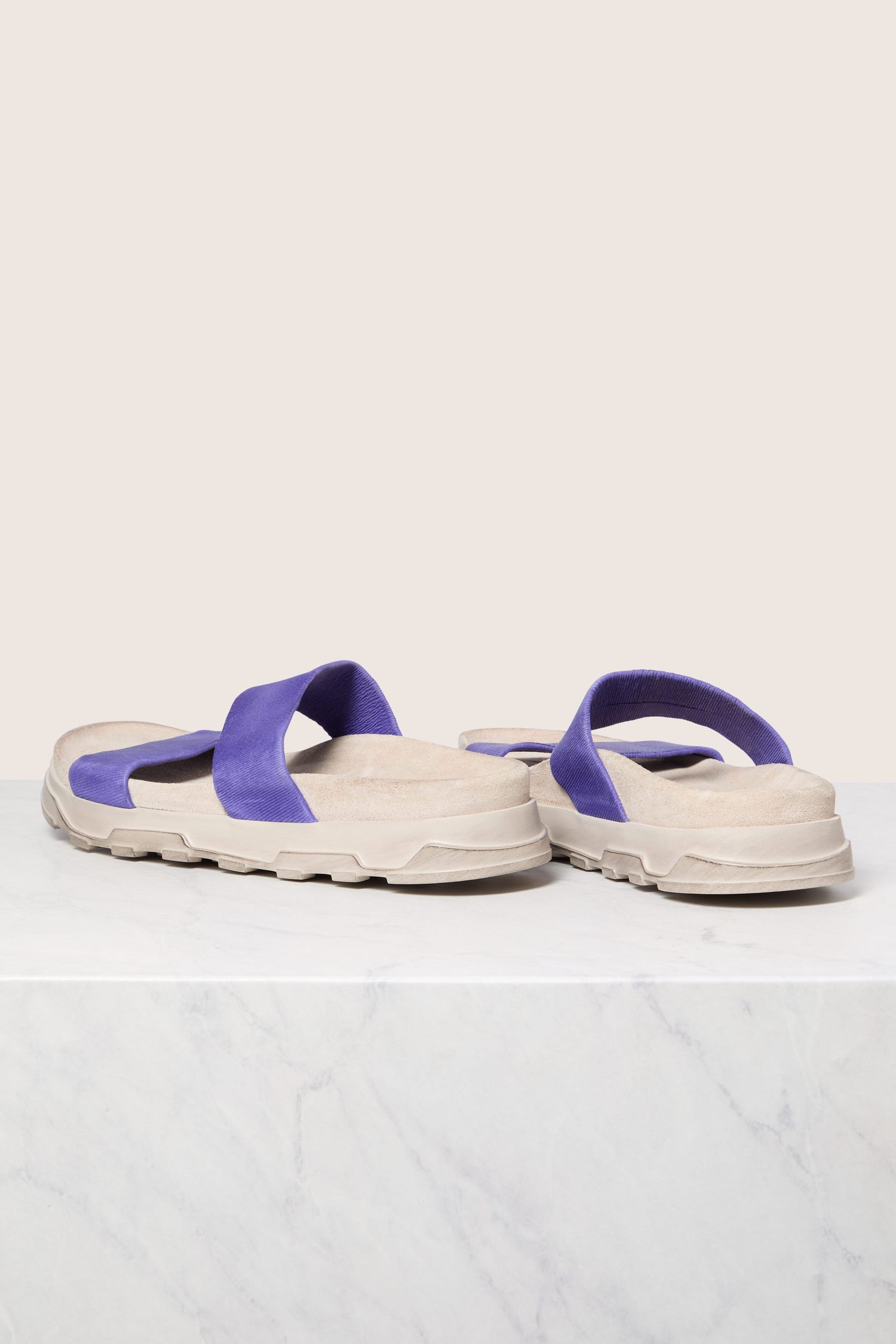 A pair of beige Stretch Leather Sliders with purple straps on a marble surface against a neutral background, showcasing Italian construction.