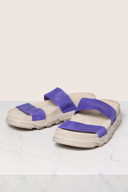 A pair of Stretch Leather Slider sandals with purple straps on a marble surface.