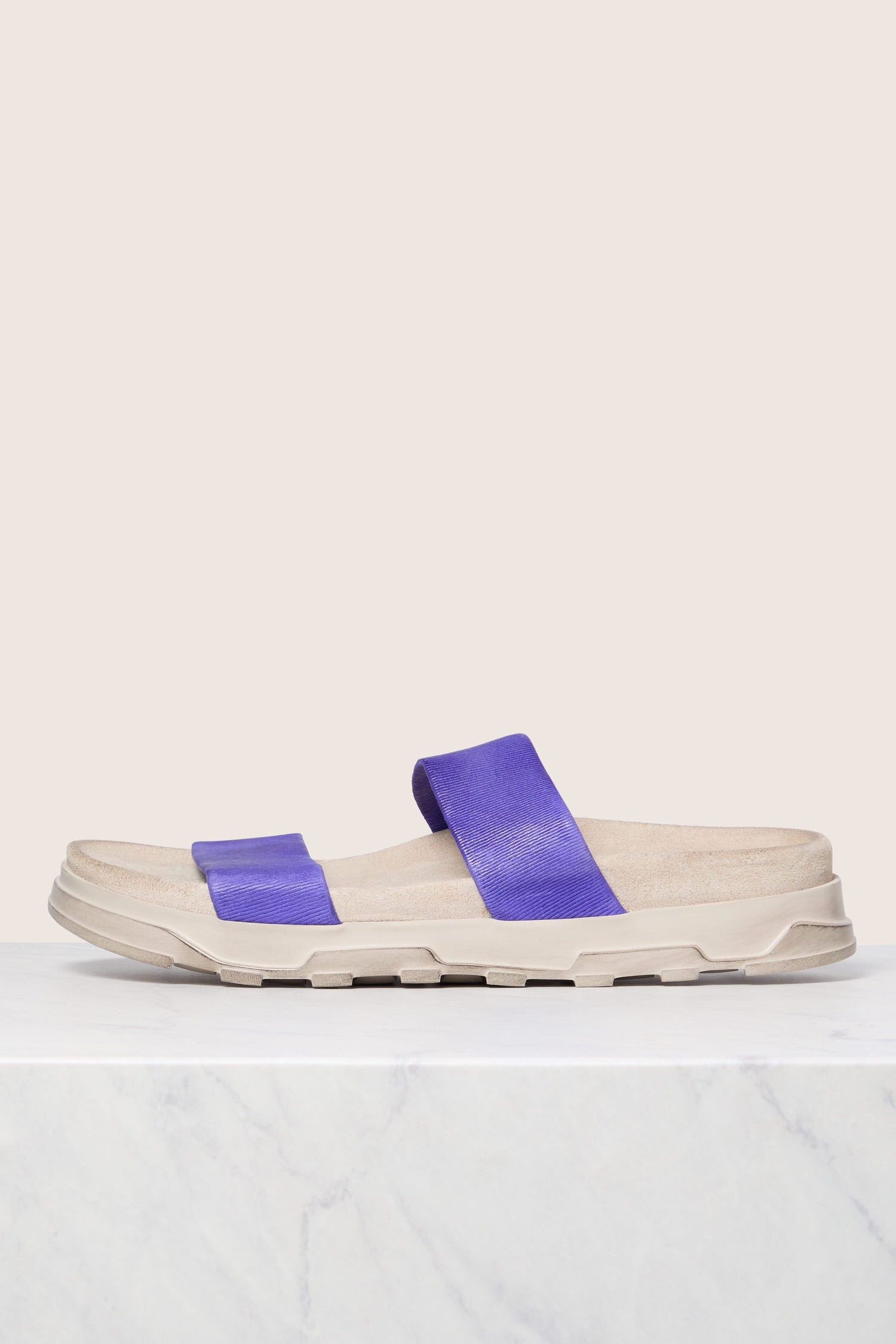 A single Stretch Leather Slider with blue straps, featuring Italian construction, displayed on a marble surface against a light background.