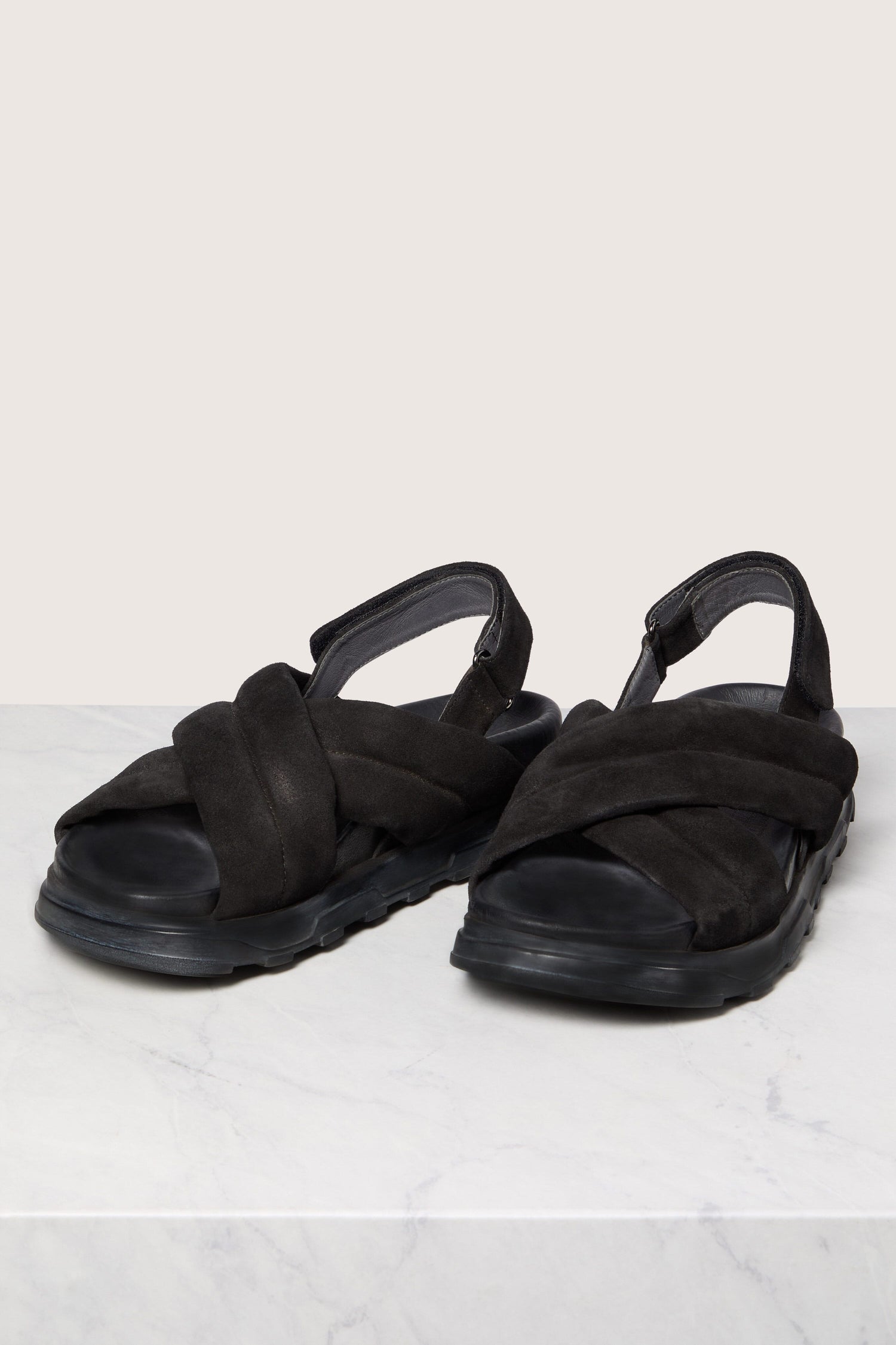 A pair of black Suede Crossover Sandals with a handmade sole on a white surface.