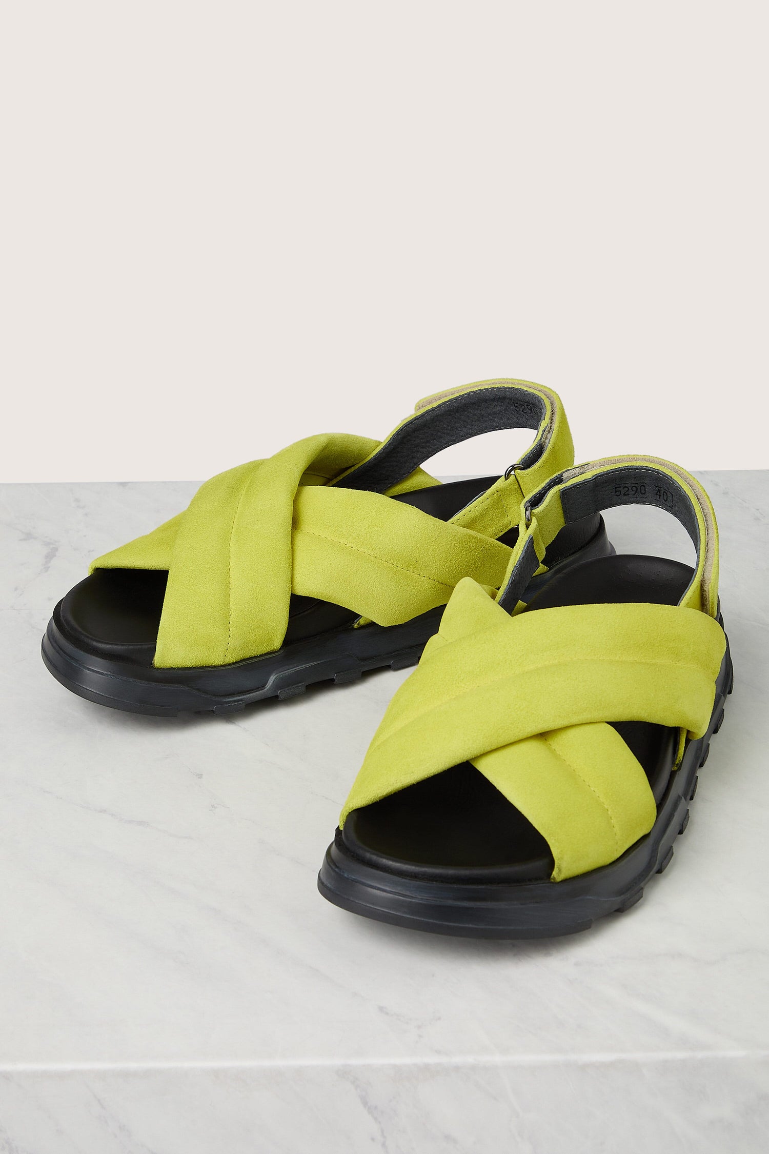 A pair of bright yellow Suede Crossover Sandals with thick straps on a marble surface, reflecting Scandinavian design.