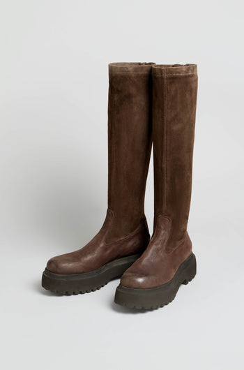 A pair of Knee High Stretch Suede Boots in a rich brown shade, featuring thick black rubber soles and rounded toes, positioned side by side on a plain light background.
