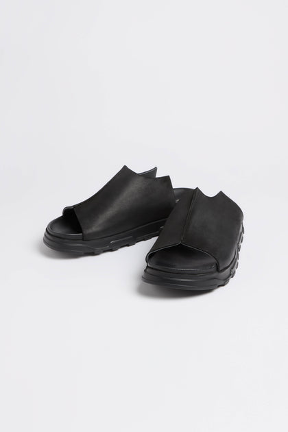 Lofina's Seam Leather Sliders, available in black, feature a cushioned sole for ultimate comfort. These open-toe sandals embody modern minimalism with their sleek design and textured sole, elegantly showcased on a white background.