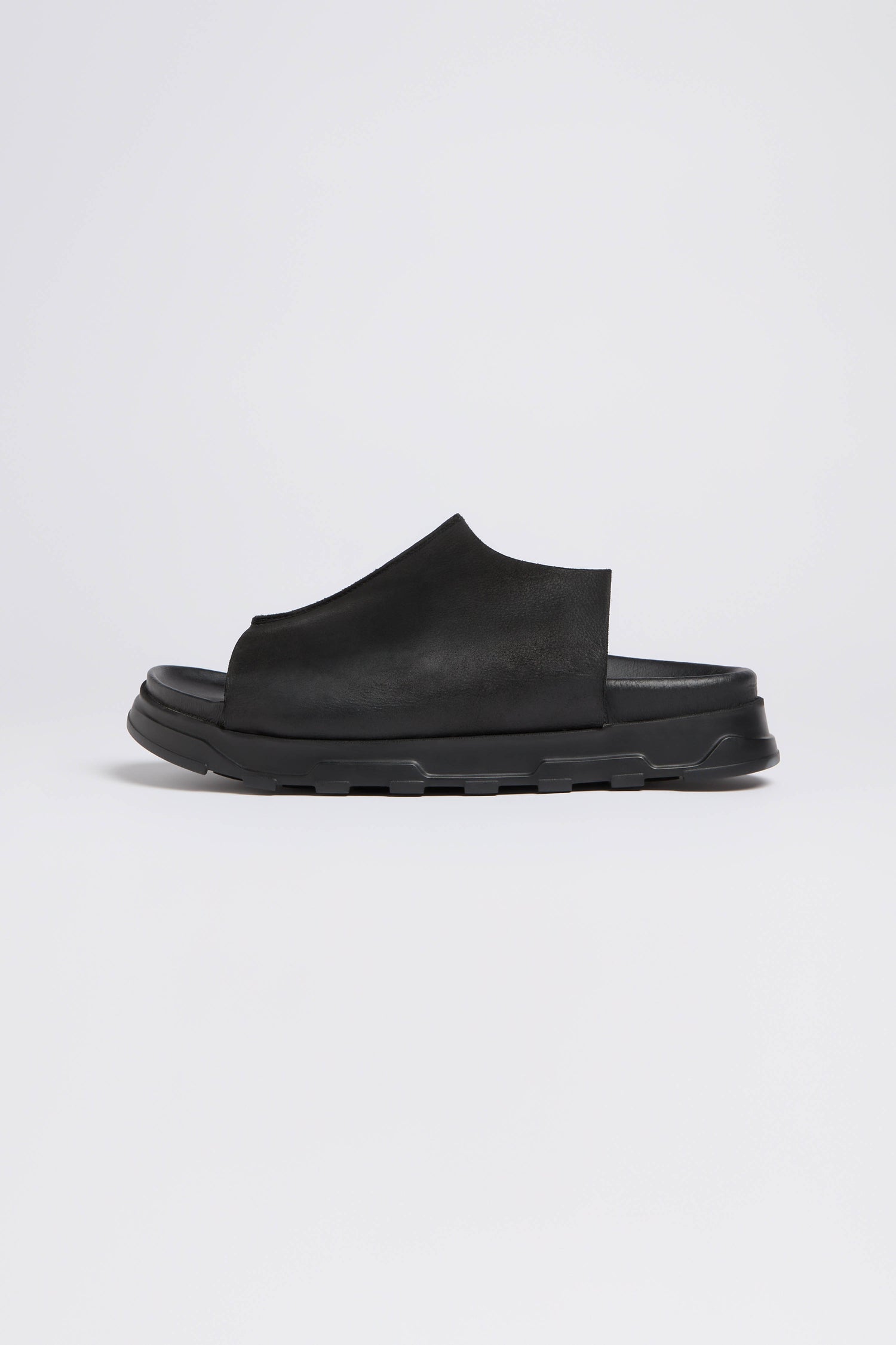 The Seam Leather Sliders from Lofina exhibit modern minimalism with a slip-on design, thick cushioned sole, and open heel, shown from the side.