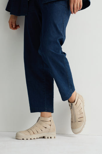 Against a white background, an individual in blue pants showcases edgy Cut Out Suede Zip Boots featuring rugged rubber soles.