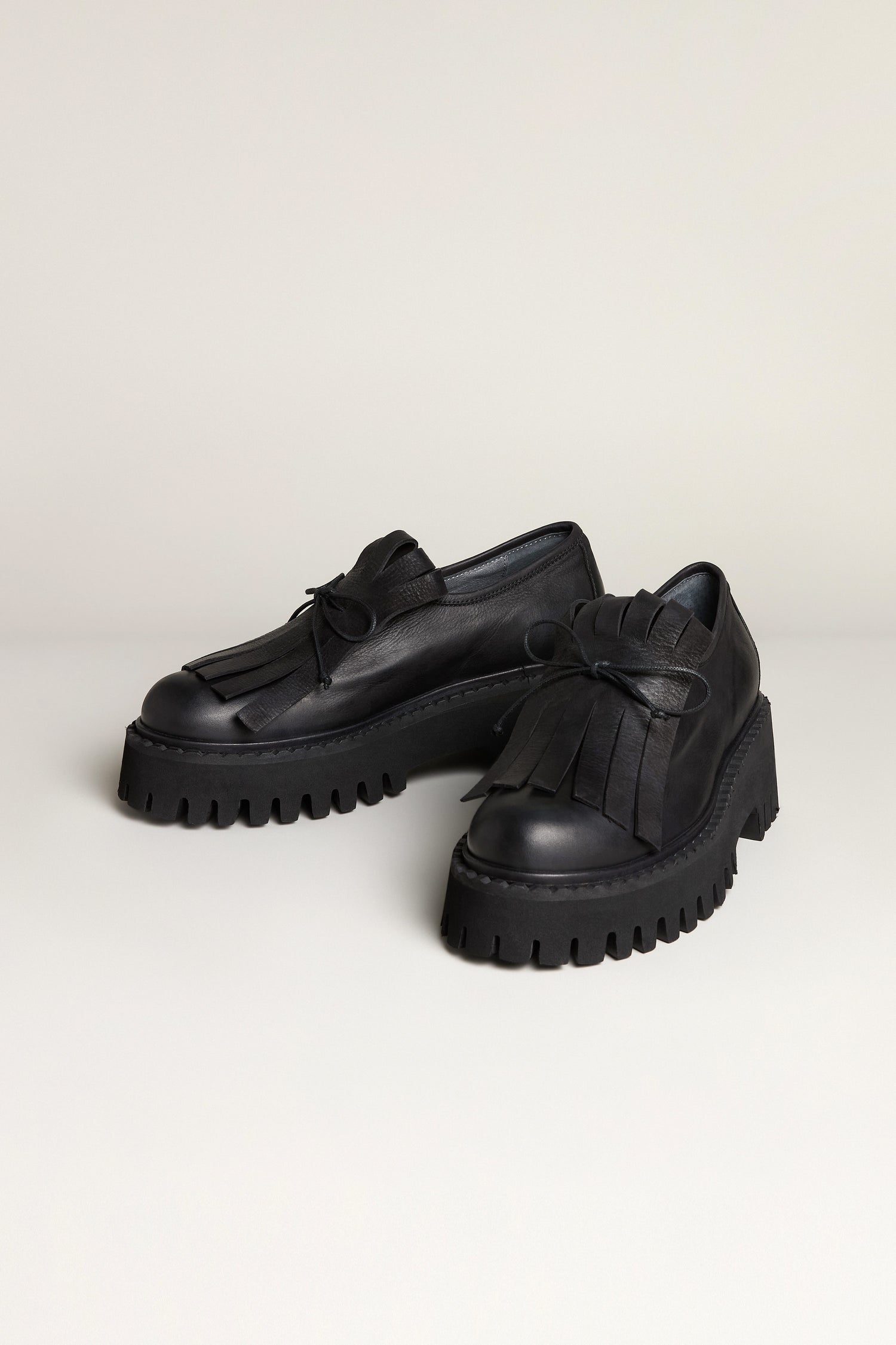 A pair of black handcrafted Fringe Top Leather Brogues with thick, ridged platform soles and decorative fringed flaps on top, displayed on a plain surface.