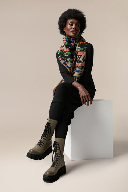 A woman wearing Platform Lace Up Leather Boots and a scarf, sitting on a white cube.