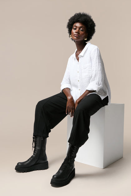 A black woman in a white shirt and black boots with Platform Lace Up Leather Boots sitting on a white cube.