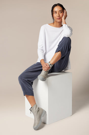 A woman is sitting on a cube wearing Zip Front Boot, complemented by minimalist style.