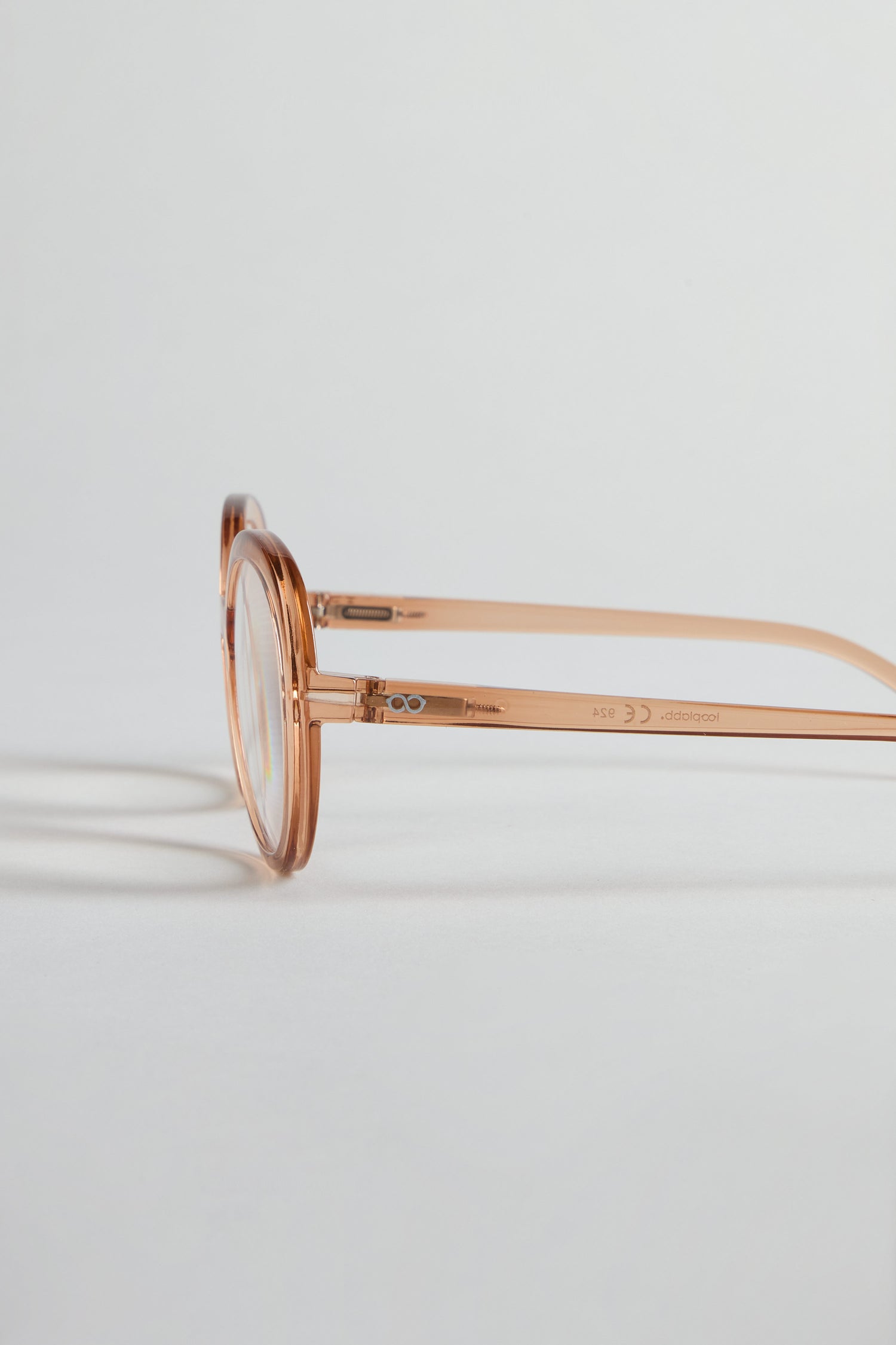 Side view of Crystal Champagne Round Reading Glasses with transparent frames and light orange arms, placed on a white surface with soft shadows.