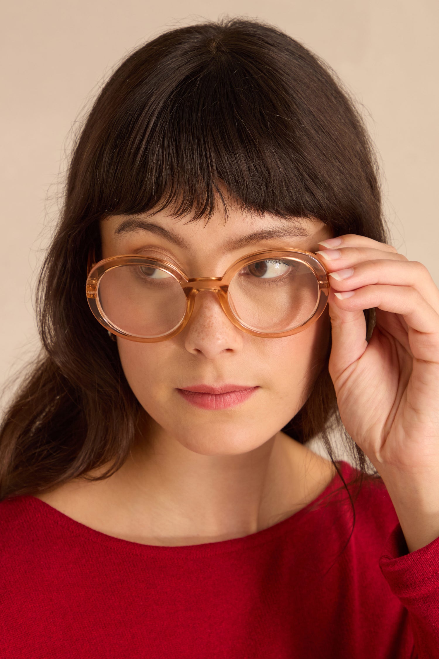 Woman in a red top looks to the side while adjusting her Crystal Champagne Round Reading Glasses with one hand.