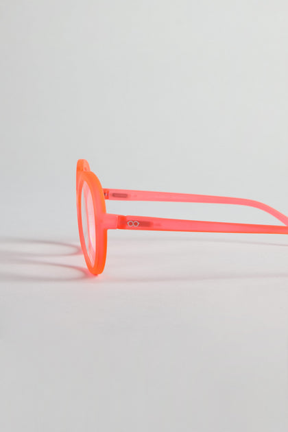 Side view of Neon Peach Round Reading Glasses featuring translucent, round frames and optician-quality lenses on a light gray background; front frame and left temple arm shown.