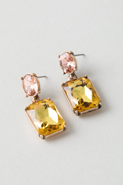 The Twin Gemstone Earrings feature oval light pink stones atop large rectangular yellow gems, all set in gold-tone metal. Their modern design adds a bold accent to any outfit.