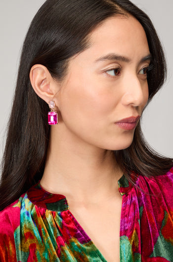 A woman with long dark hair wears a vibrant multicolored velvet top and striking Twin Gemstone Earrings featuring large pink stones, gazing to the side.