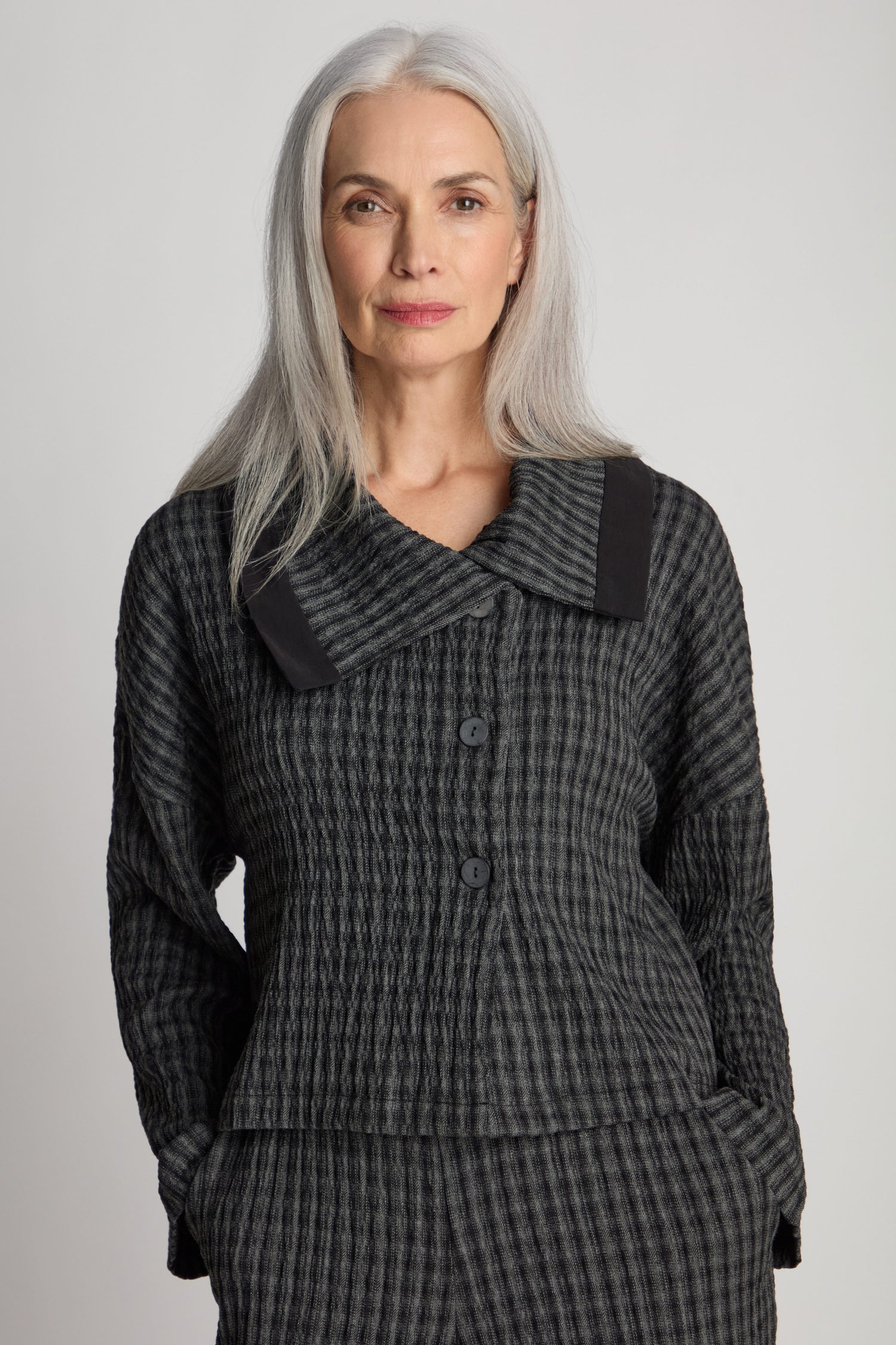 A woman with long gray hair stands against a plain background, wearing a Check Shawl Collar Jacket in a dark, textured pattern.