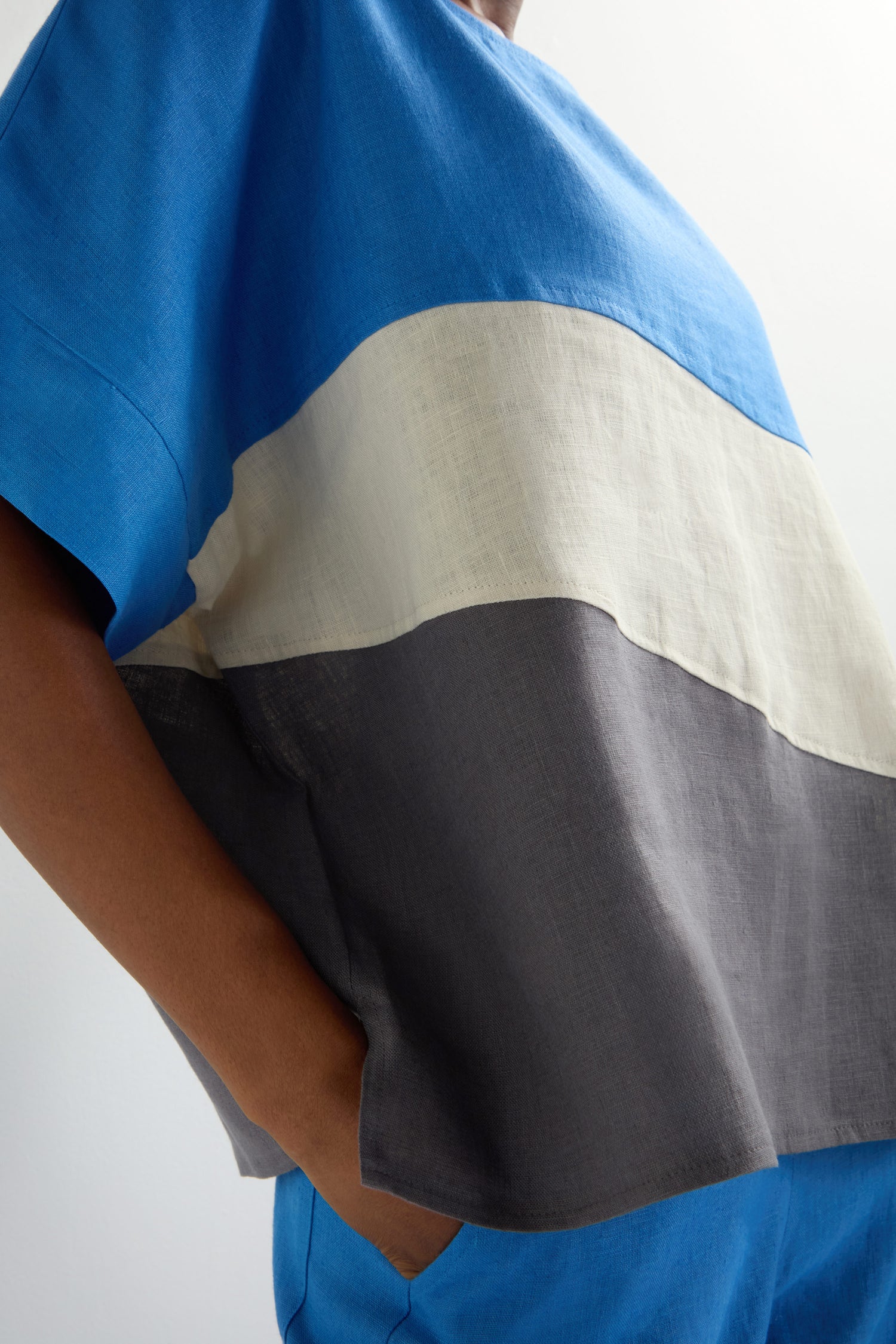 Wearing the Colour Block Top, featuring eye-catching blue, white, and gray sections, the person stands confidently with hands in pockets, exuding effortless style.