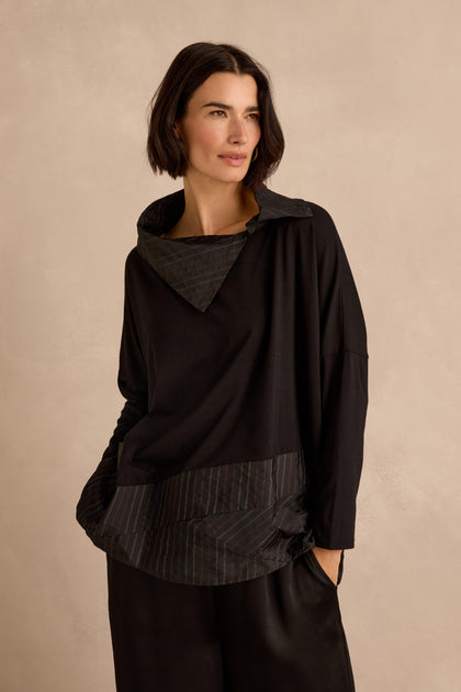 A woman wearing the Stripe Jersey Taffeta Tunic—an oversized, long-sleeved brown and black striped top—paired with black pants, stands against a plain beige background.