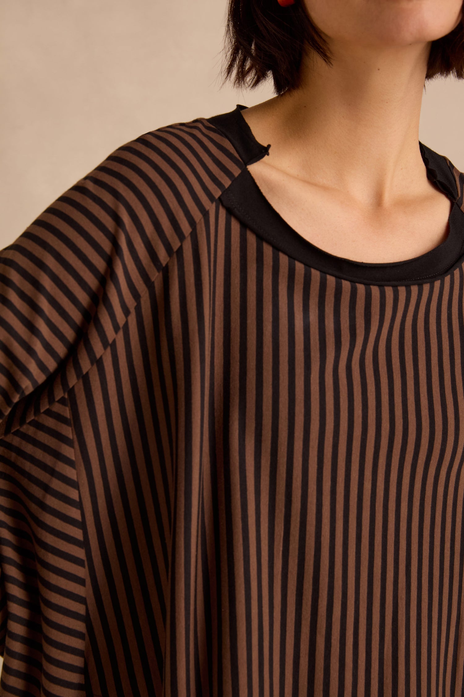 A person is shown wearing the Stripe Jersey Wide Neck Tunic—a loose top featuring black and brown vertical stripes, a black collar, and crafted from cotton stretch jersey. Only their shoulders, chest, and lower face are visible.