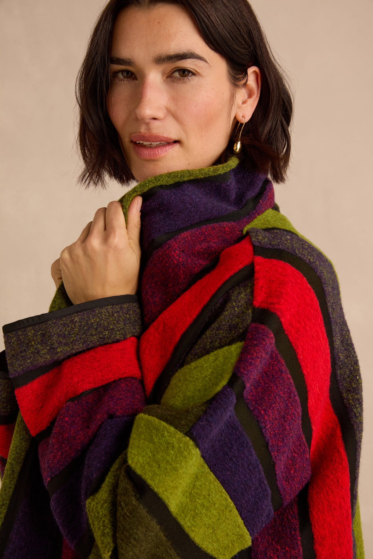 A person with short brown hair wears the Sheer Stripe Jacket in vibrant red, green, and purple stripes, holding the collar and looking at the camera with a neutral expression.