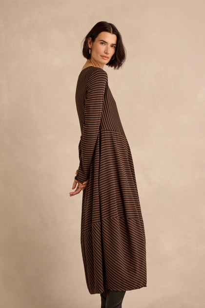 Woman with short dark hair and purple earrings wears the Draped Stripe Jersey Dress, standing against a neutral background and looking confidently at the camera.