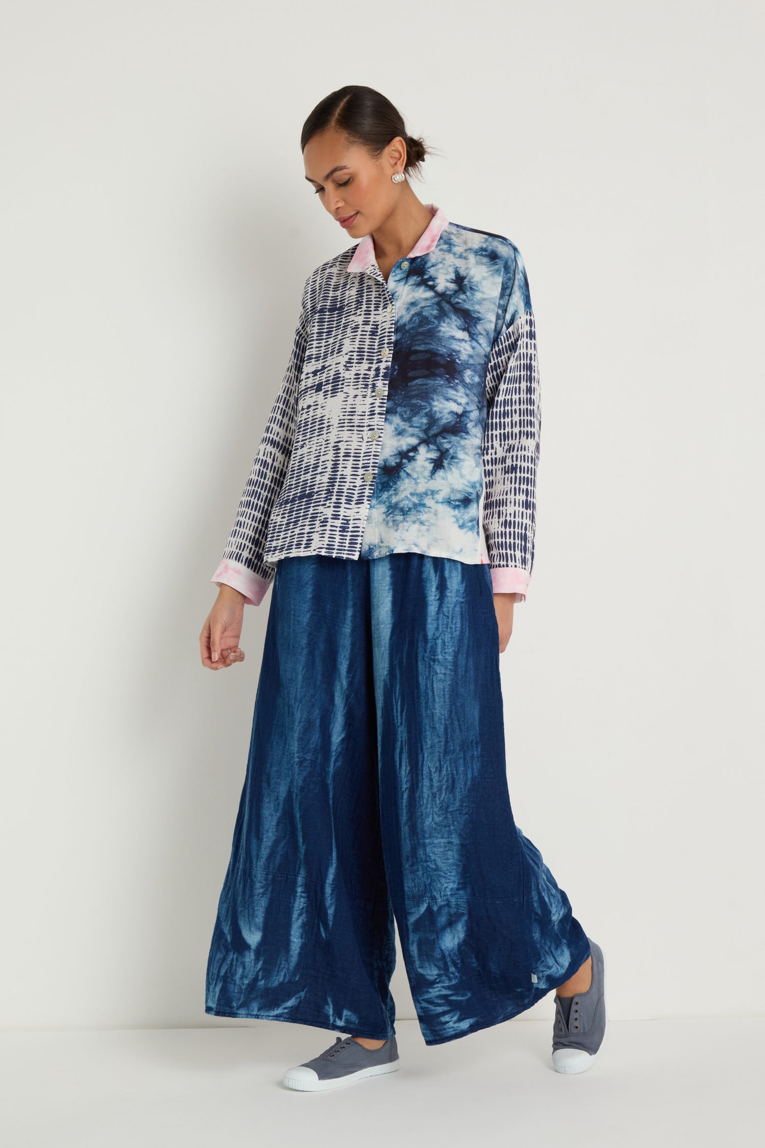 A woman stands against a white background wearing the Floral Back Easy Shirt, wide-leg blue pants, and gray sneakers.