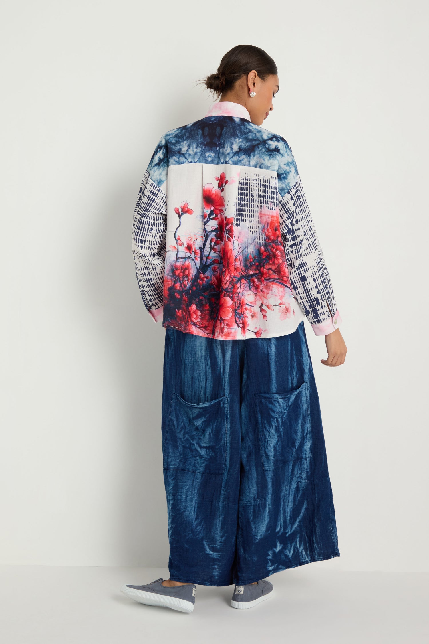 A person faces away in the Floral Back Easy Shirt featuring blue, white, and red abstract floral patterns, paired with loose blue pants against a plain white background.