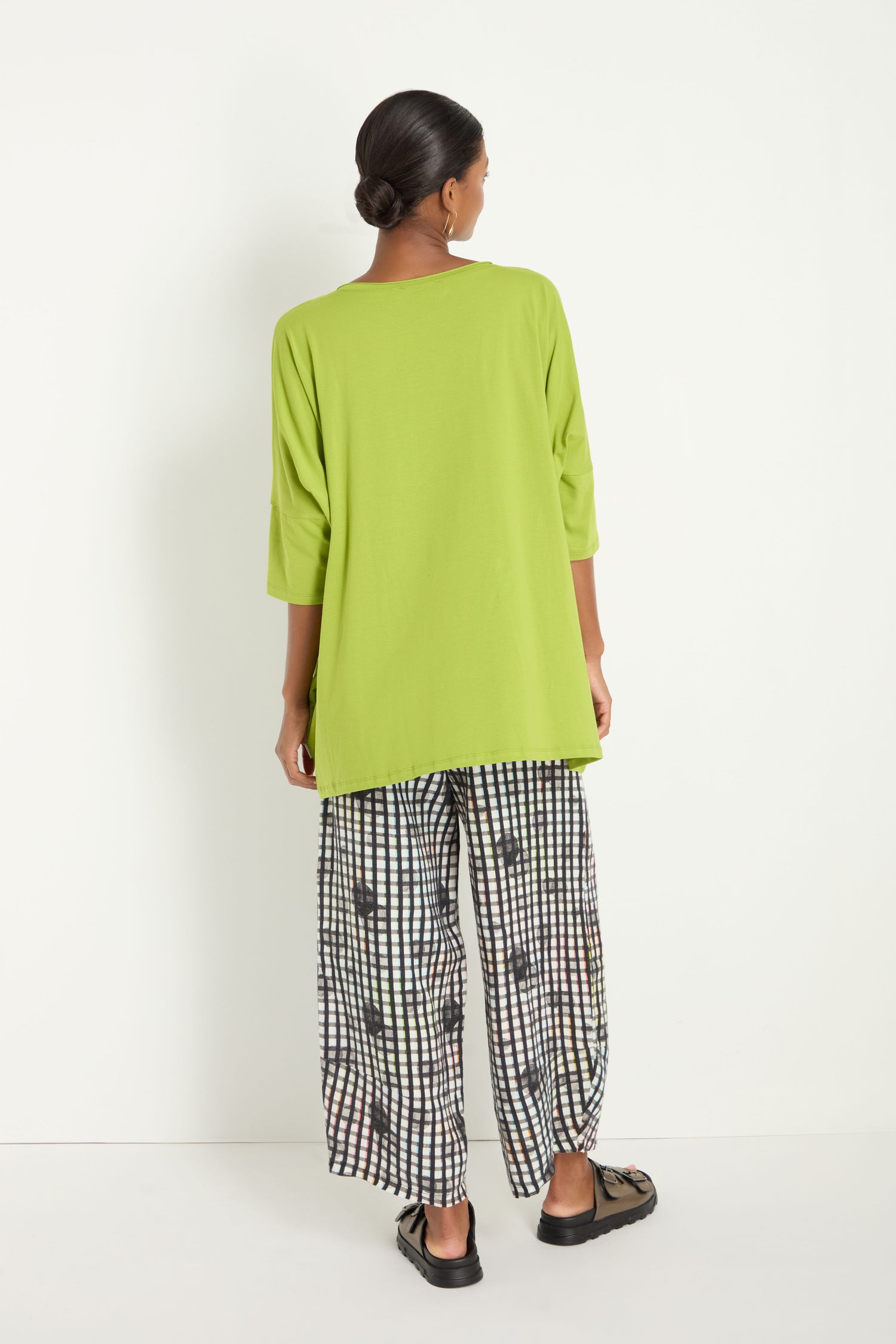 A person faces away, wearing the Tuck Hem Swing Lime Tunic paired with black and white checkered wide-leg pants and black shoes, set against a plain white background.
