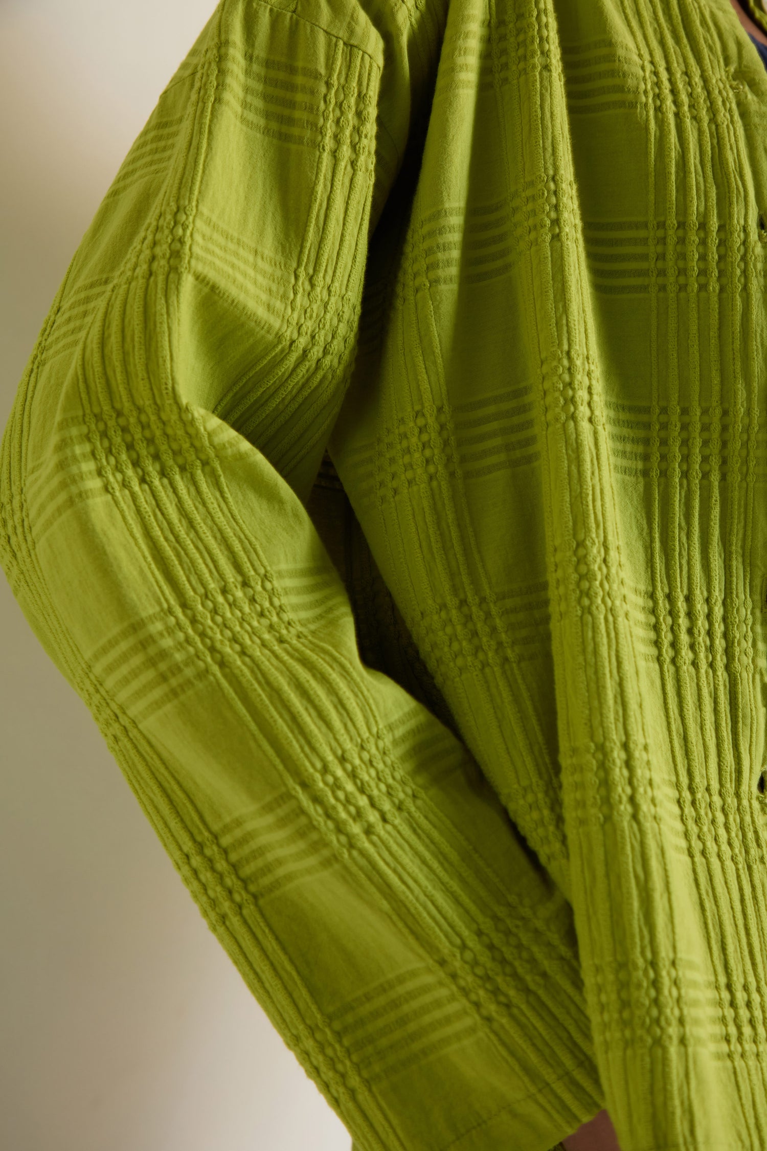 Close-up of a person wearing the Self Check Lime Boxy Shirt, a textured, light green cotton long sleeve with a subtle self-check pattern and relaxed silhouette.
