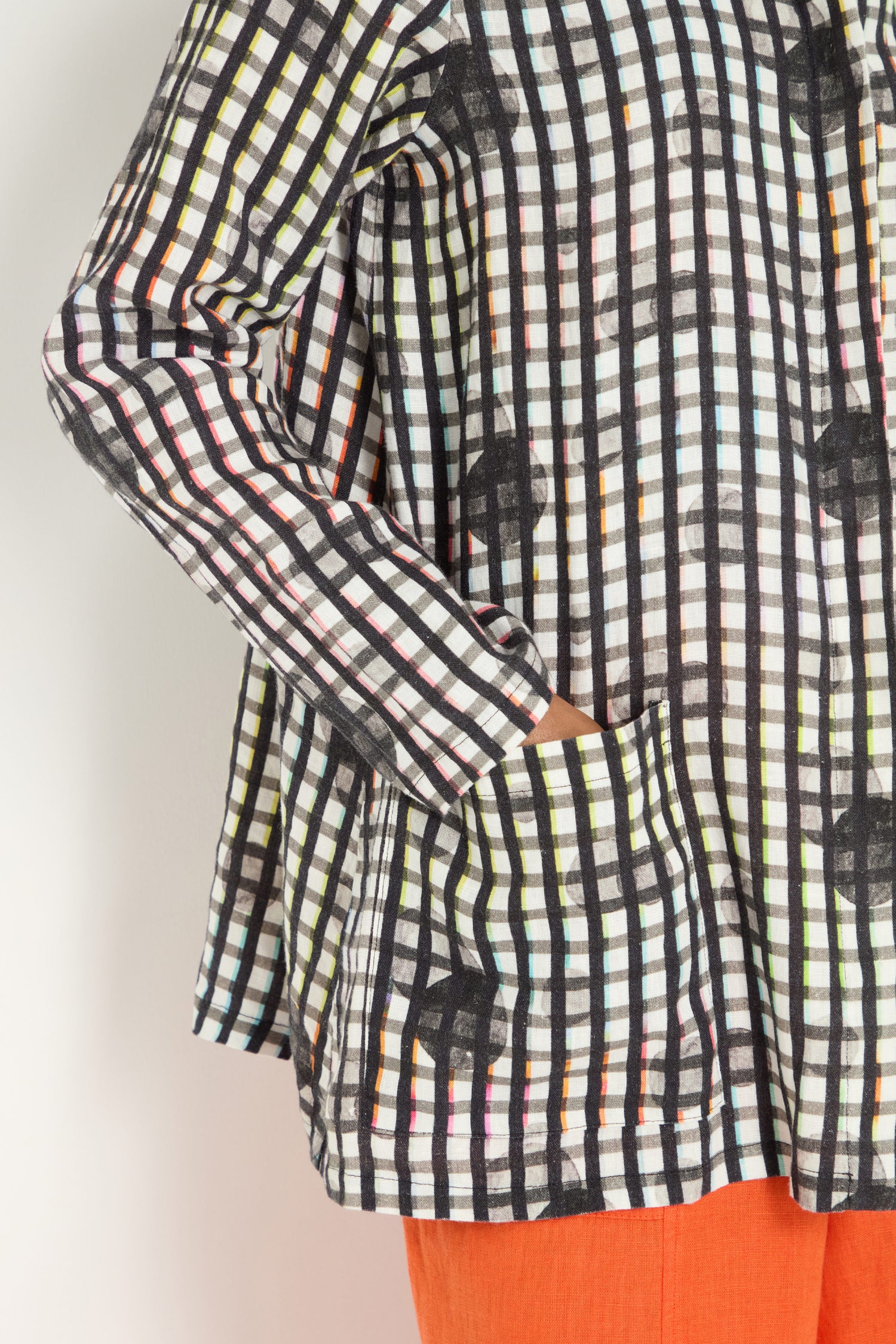 A person wearing a relaxed fit, long-sleeve Check Dot Linen Shirt with a front pocket and bright orange pants, photographed from the shoulder to mid-thigh.