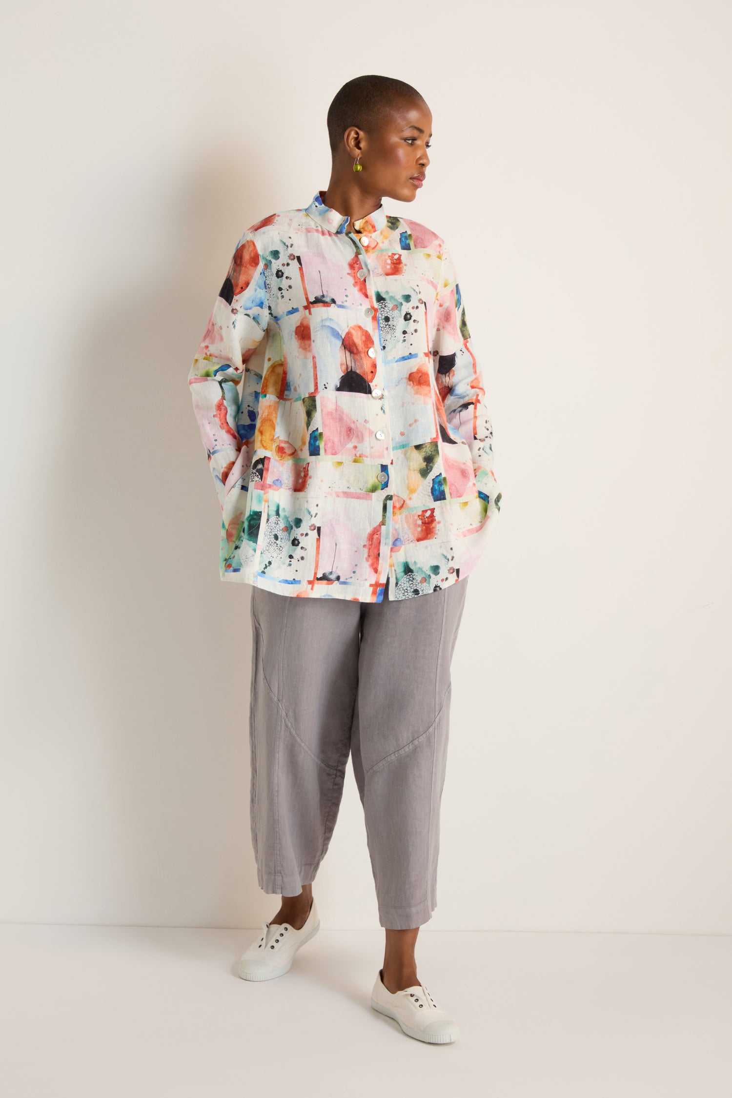 A person stands against a plain background wearing the Watercolour Linen Print Shirt, paired with loose gray pants and white sneakers.
