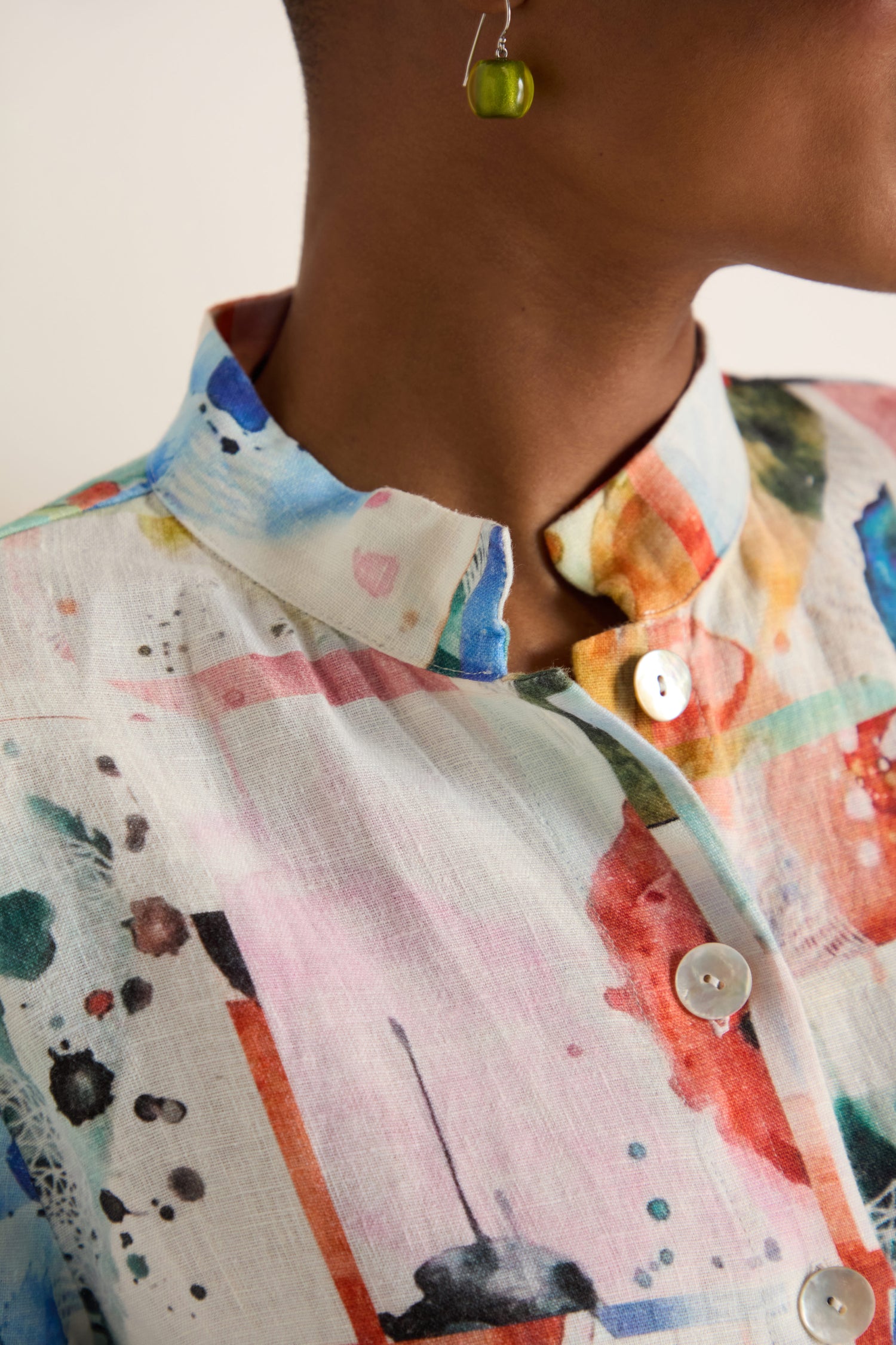Close-up of a person wearing the Watercolour Linen Print Shirt, featuring a relaxed fit, white buttons, and paired with a green cube-shaped earring.