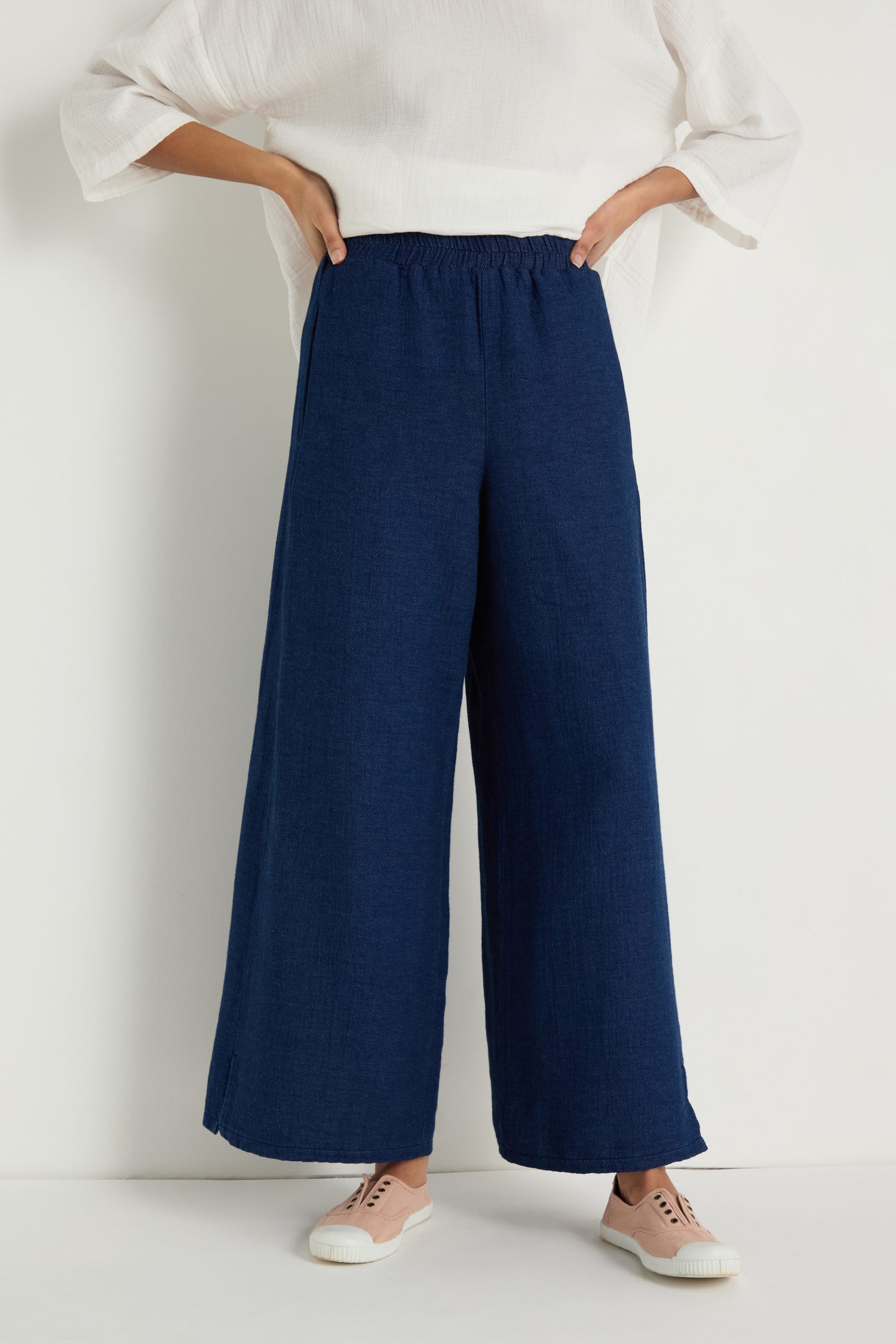 Person wearing a white top, Wide Leg Slit Trousers with an elastic waistband, and light pink sneakers, standing against a plain white background.