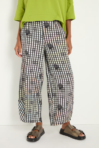 A person stands against a plain white background wearing a loose lime green top, brown sandals, and black and white Check Dot Linen Trousers with a relaxed straight leg.