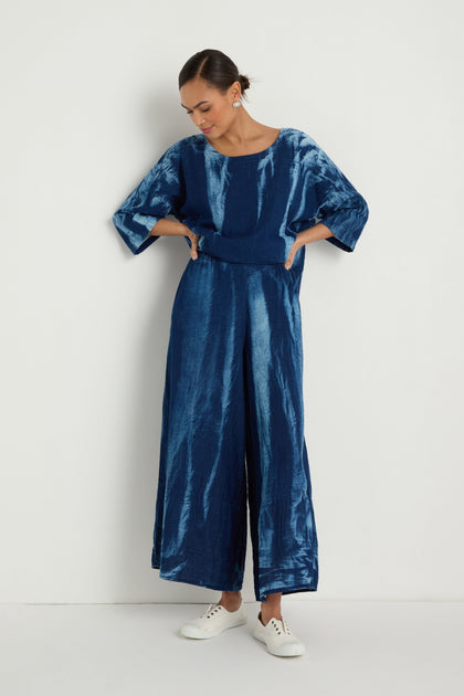 Woman wears Soft Denim Pocket Trousers with a loose-fitting, tie-dye blue top and white sneakers, standing against a plain white background.