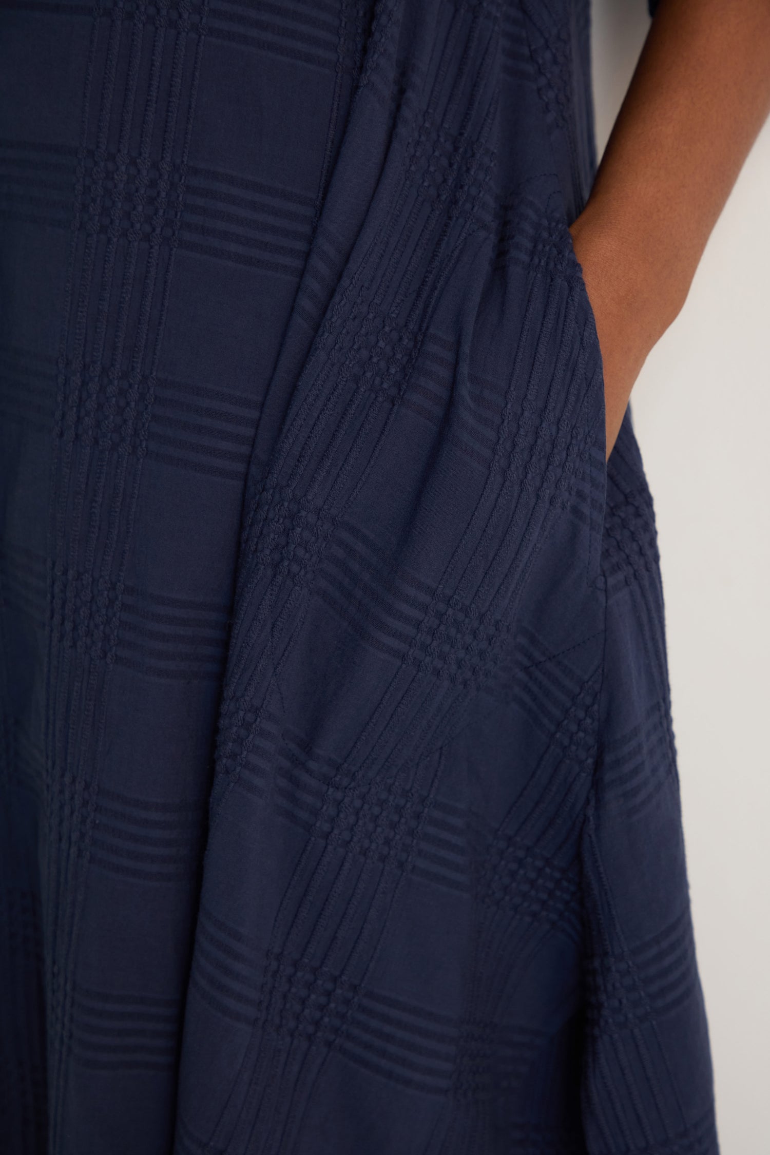Close-up of a hand in the pocket of the Self Check Navy Shirt Dress, featuring a textured check pattern in navy blue cotton.