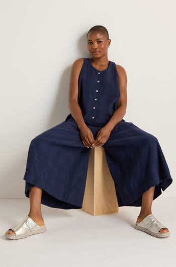 A person wearing the Self Check Sleeveless Jumpsuit sits on a wooden block against a plain white background.