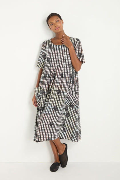 Woman in a Check Dot Pleated Linen Dress with a black and white grid pattern, loose fit, knee-length, and short sleeves, standing against a plain white background.