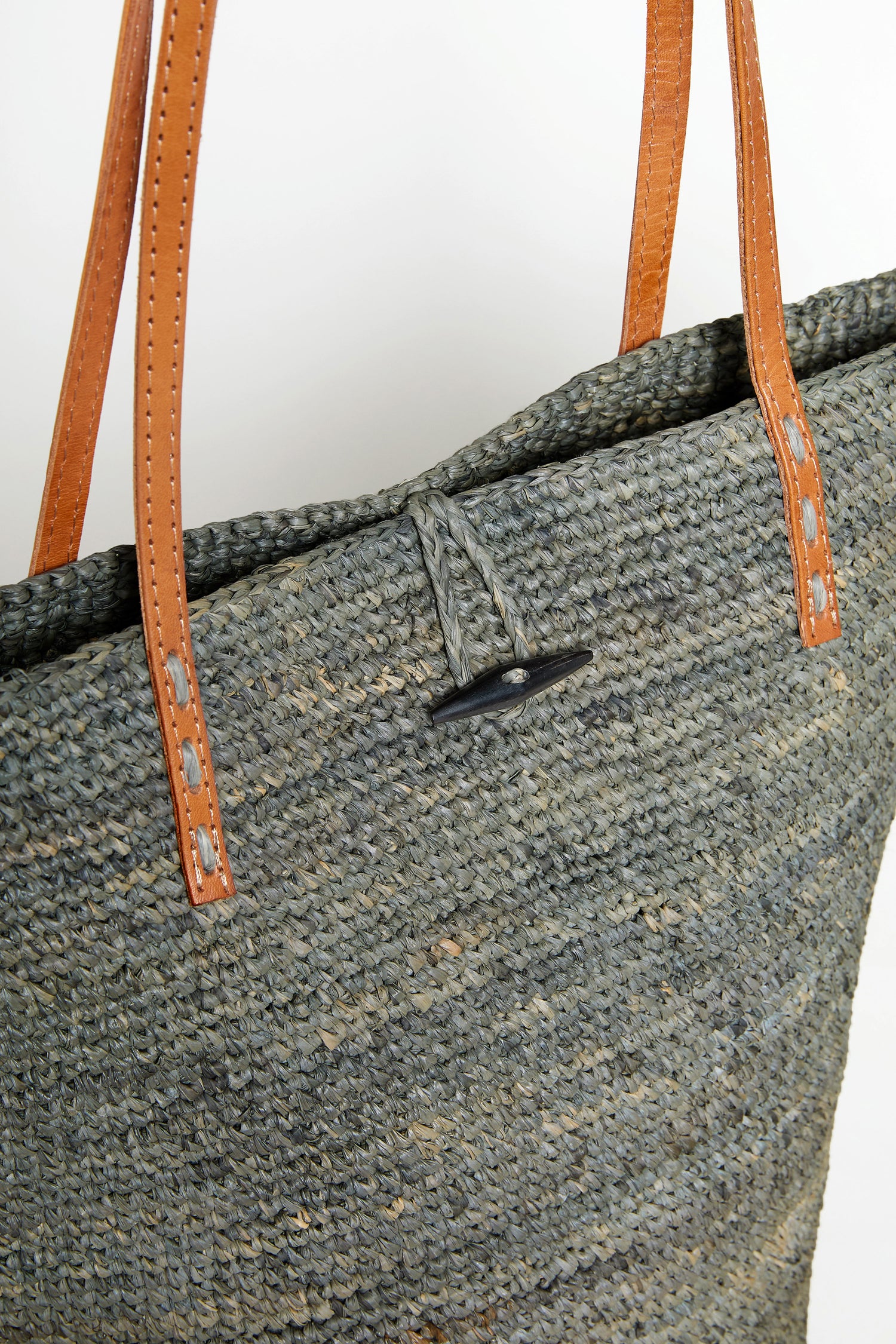 Close-up of the Ilana Raffia Basket, showcasing its brown leather handles and black toggle closure against a plain background.